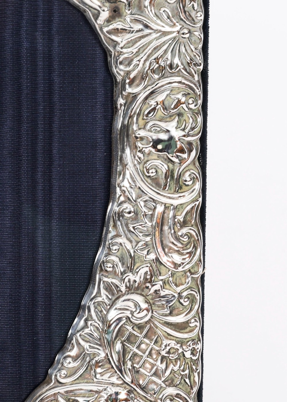 An antique sterling silver double aperture photo frame featuring heart-shaped openings, intricate repousse floral scrollwork, and cherub details mounted on dark velvet. View VII