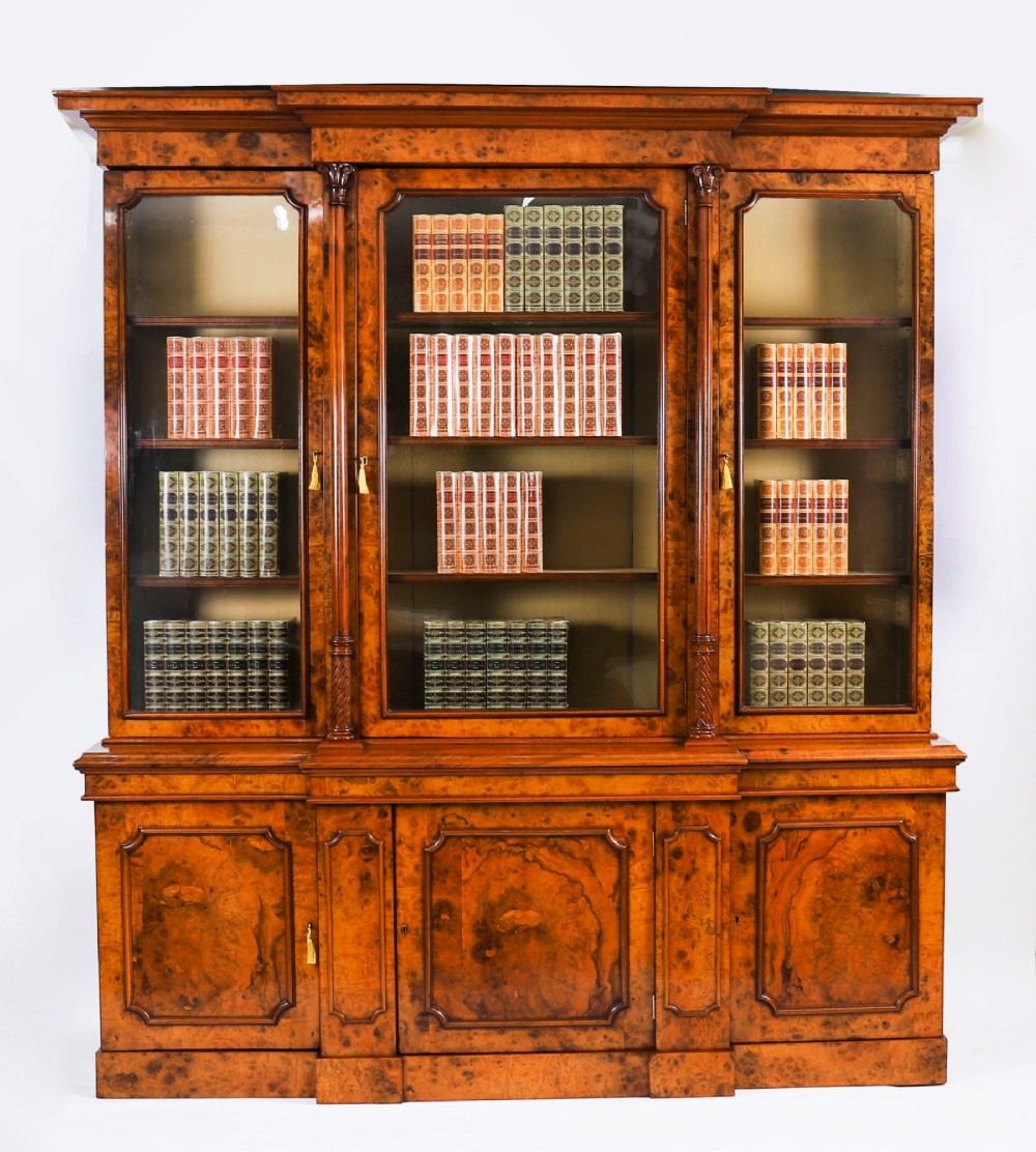 A mid-19th-century Victorian burr walnut breakfront bookcase featuring three upper glazed doors, turned pilasters, and three lower panelled cupboard doors.