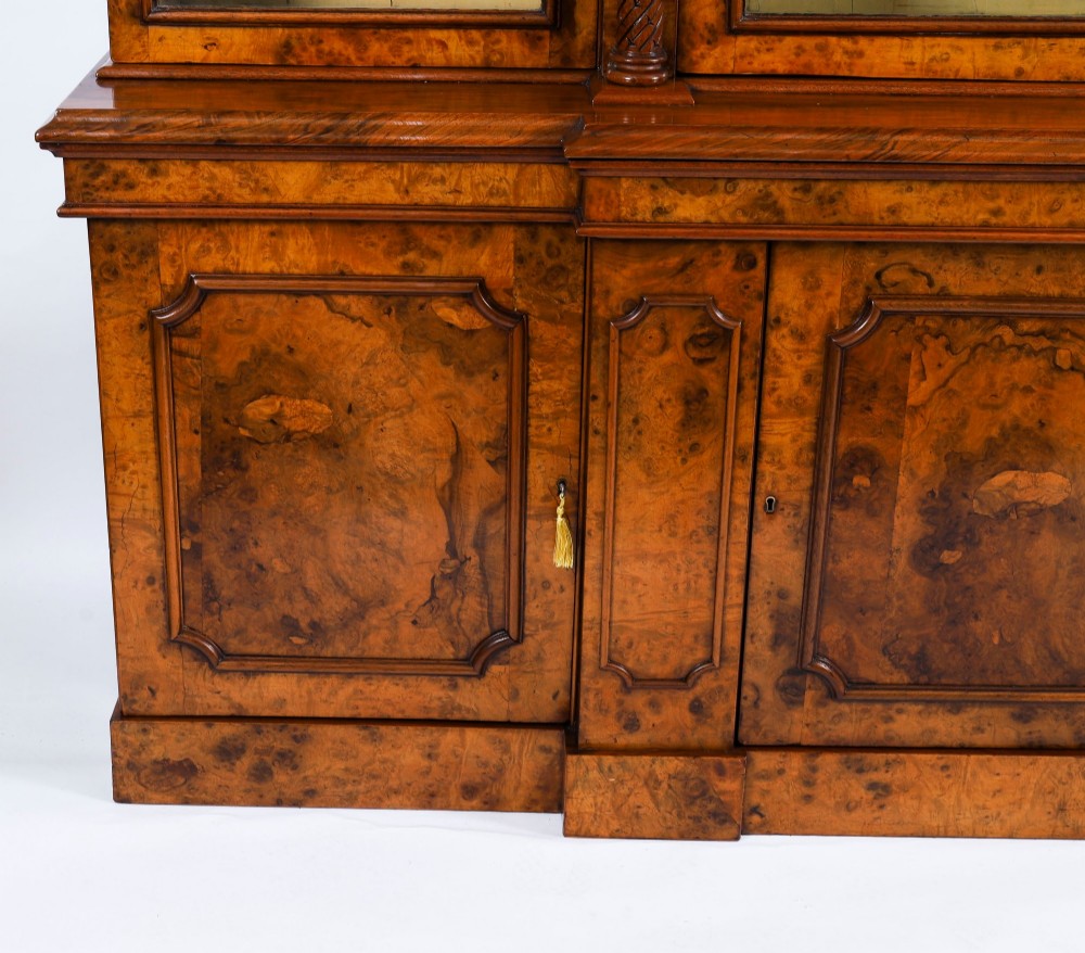 A mid-19th-century Victorian burr walnut breakfront bookcase featuring three upper glazed doors, turned pilasters, and three lower panelled cupboard doors. View VI