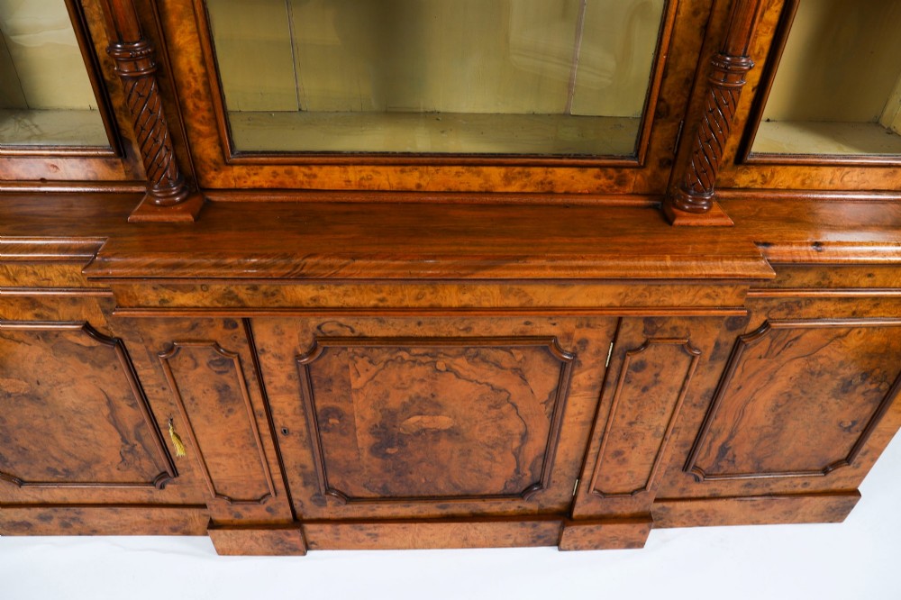 A mid-19th-century Victorian burr walnut breakfront bookcase featuring three upper glazed doors, turned pilasters, and three lower panelled cupboard doors. View VII