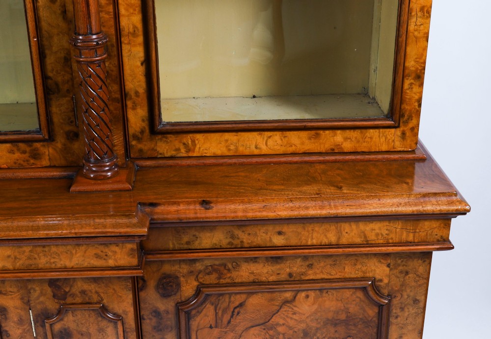 A mid-19th-century Victorian burr walnut breakfront bookcase featuring three upper glazed doors, turned pilasters, and three lower panelled cupboard doors. View VIII