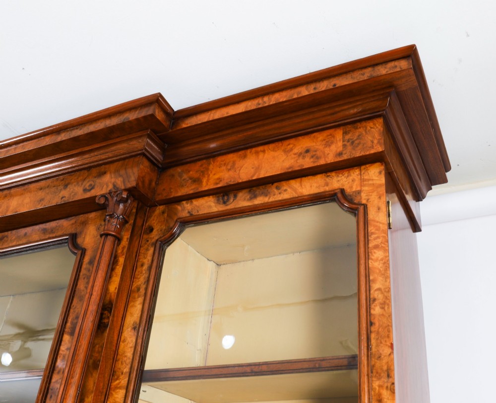 A mid-19th-century Victorian burr walnut breakfront bookcase featuring three upper glazed doors, turned pilasters, and three lower panelled cupboard doors. View XIV