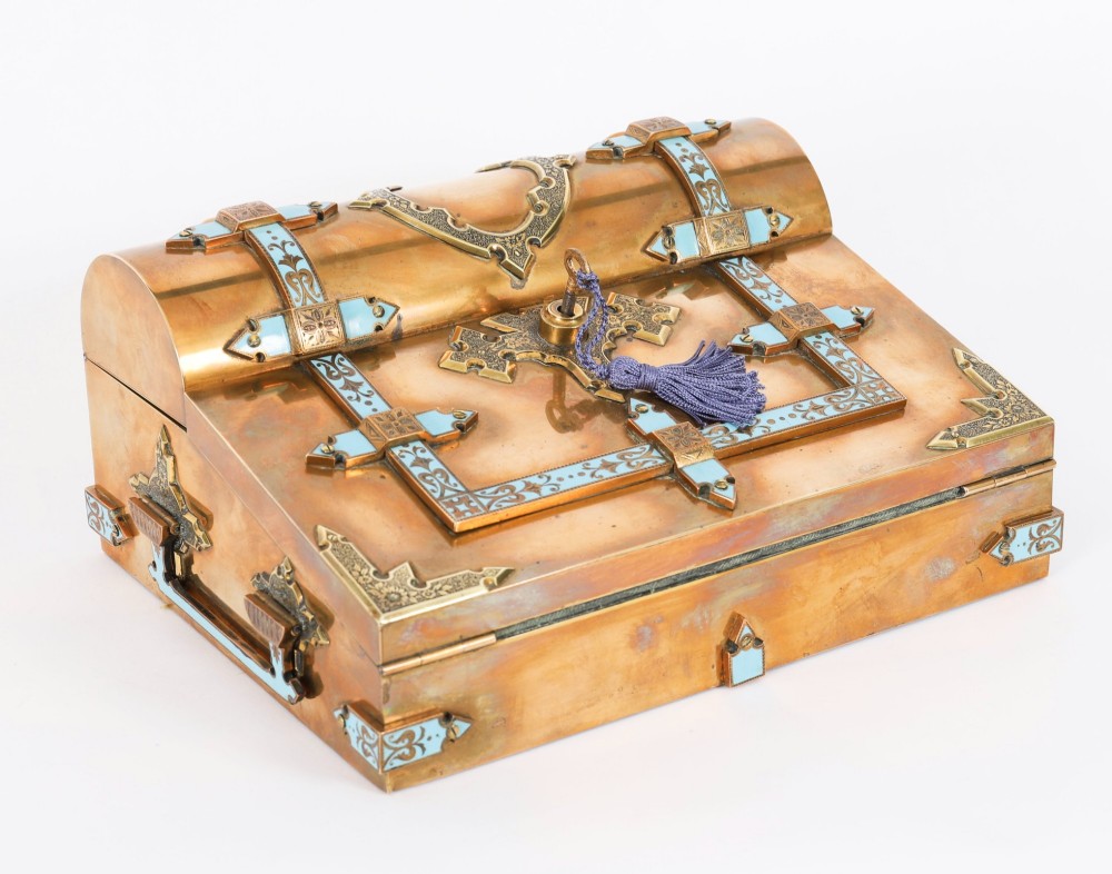 A Victorian gilt brass and turquoise champleve enamel writing slope featuring a domed upper compartment, a sloped front lid, and a key with a purple tassel in the lock.