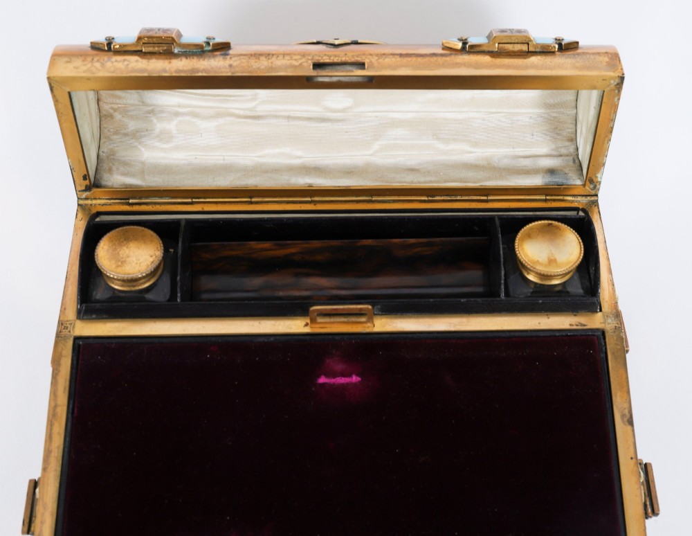 A Victorian gilt brass and turquoise champleve enamel writing slope featuring a domed upper compartment, a sloped front lid, and a key with a purple tassel in the lock. View IX