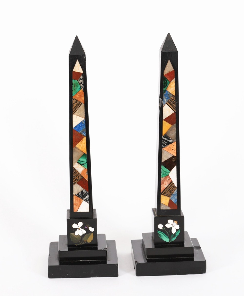A pair of antique black marble obelisks featuring colourful geometric stone inlays along the shaft and floral inlaid detail on stepped square bases.