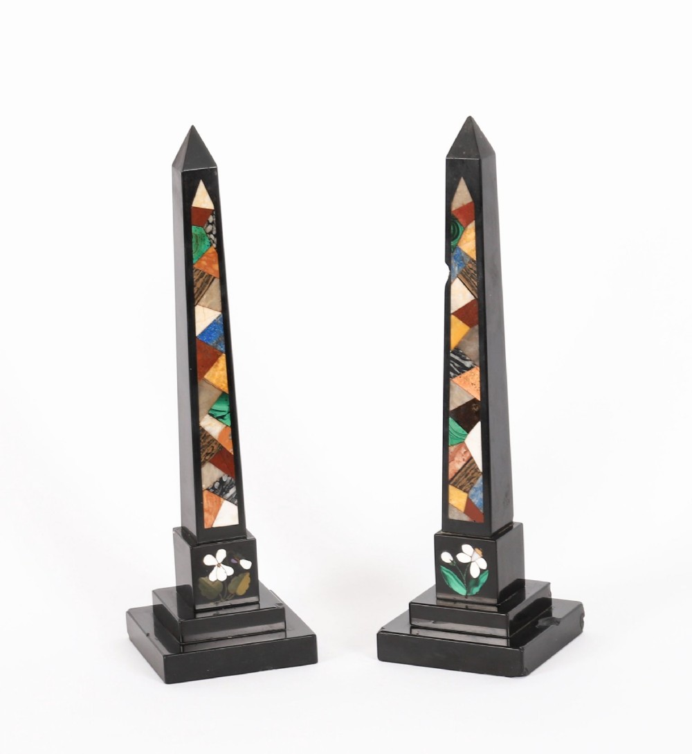 A pair of antique black marble obelisks featuring colourful geometric stone inlays along the shaft and floral inlaid detail on stepped square bases. View II