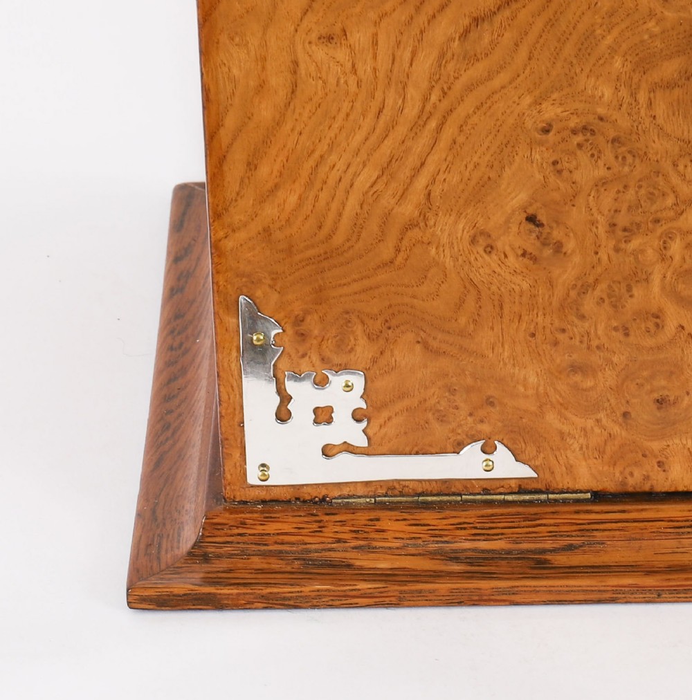 A 19th-century Victorian figured oak three-bottle tantalus open to reveal three cut glass decanters, a fitted cribbage board, and a drop-front drawer containing a silver-plated tray and playing cards. View X