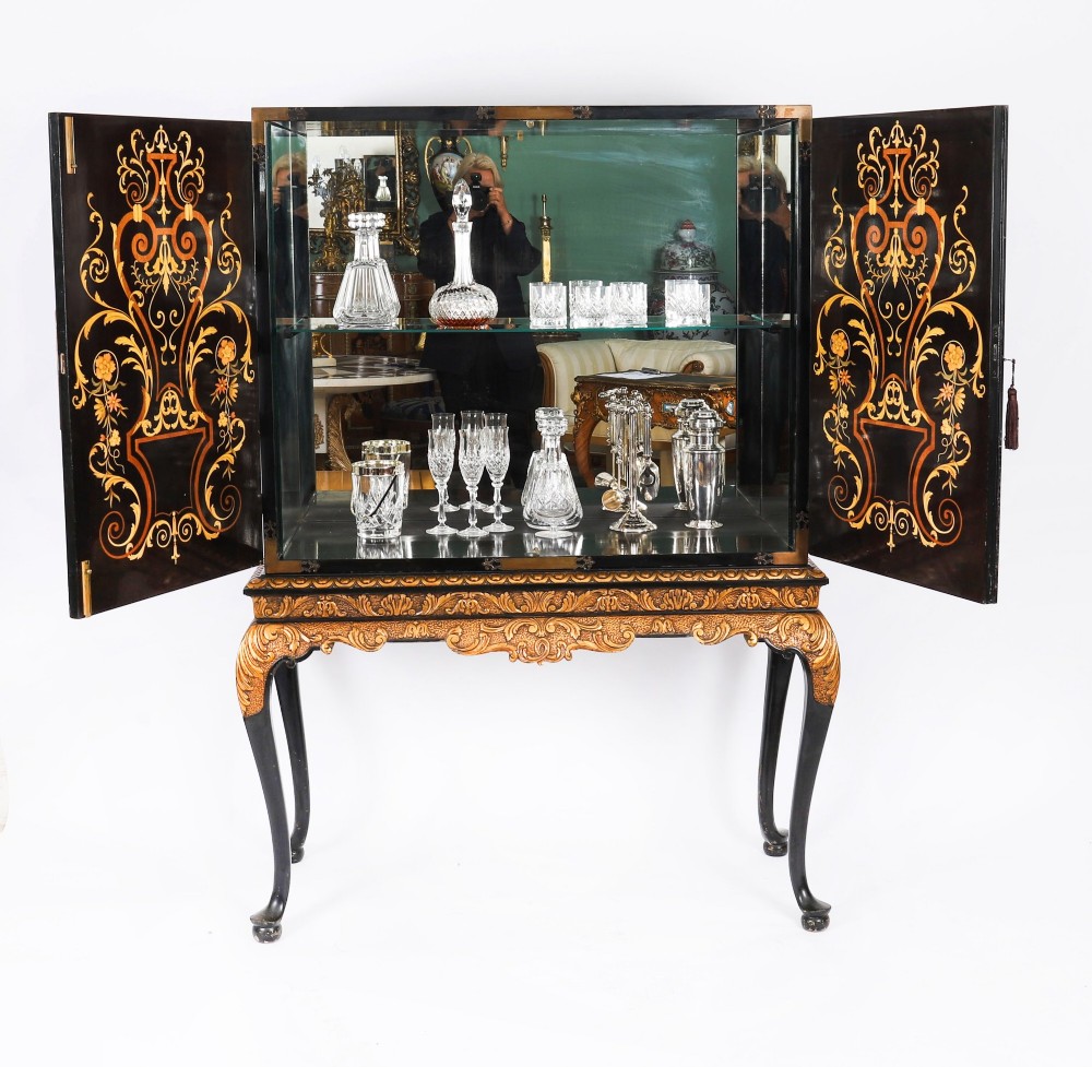 A black lacquered and inlaid wooden cocktail cabinet featuring ornate floral marquetry and decorative brass straps, resting on a carved gilded stand with cabriole legs. View II