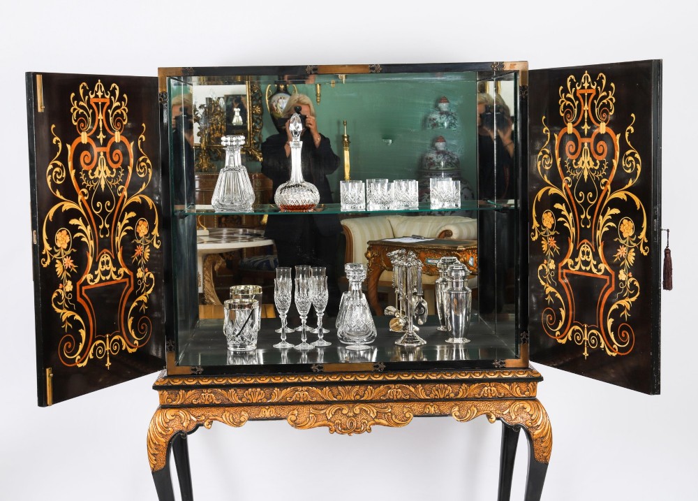 A black lacquered and inlaid wooden cocktail cabinet featuring ornate floral marquetry and decorative brass straps, resting on a carved gilded stand with cabriole legs. View IV