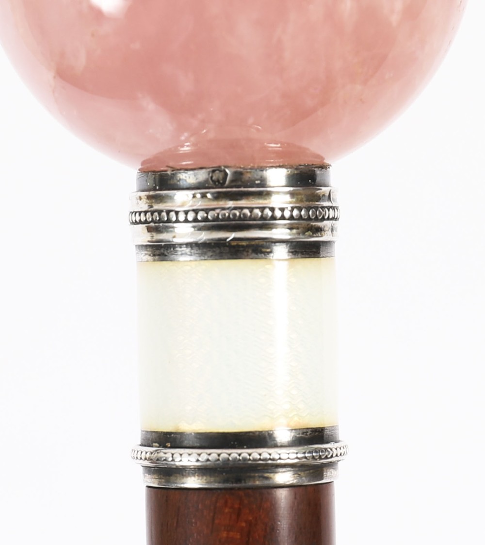An antique walking stick featuring a spherical pink quartz pommel set above a white enamel collar with silver beaded borders and a dark wood shaft. View V