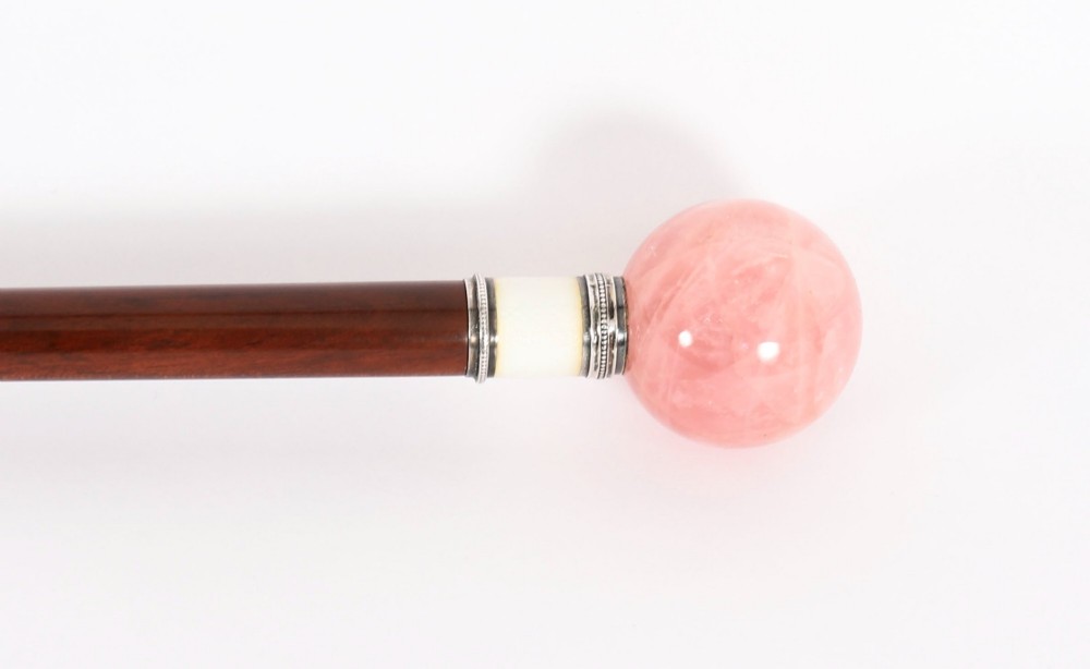 An antique walking stick featuring a spherical pink quartz pommel set above a white enamel collar with silver beaded borders and a dark wood shaft. View VI