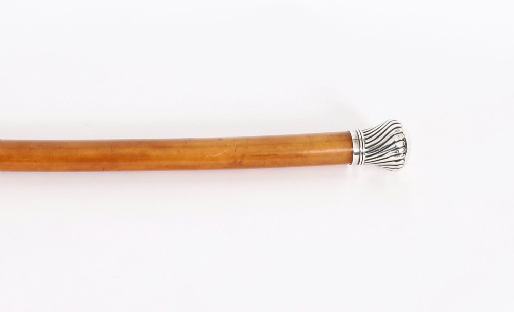 Victorian walking cane featuring an engraved sterling silver pommel with spiralled fluting mounted on a light wood shaft. View V