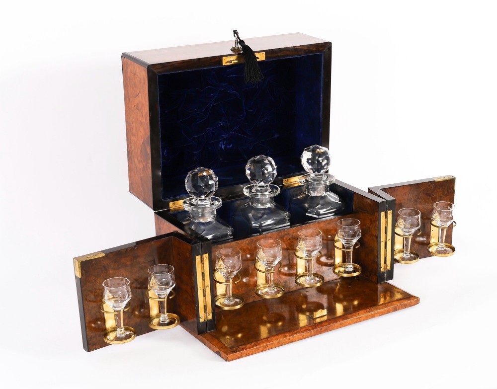 An open and closed 19th-century Victorian burr walnut tantalus box containing three cut crystal decanters, brass-mounted liqueur glasses, and a deep blue velvet lining. View II