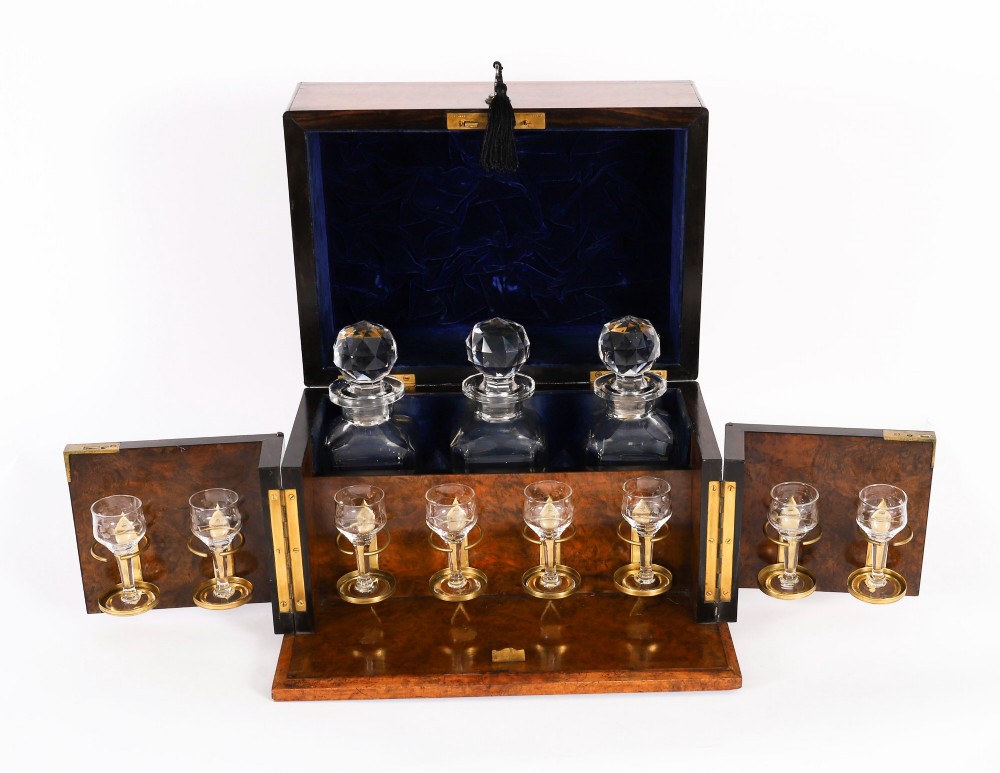 An open and closed 19th-century Victorian burr walnut tantalus box containing three cut crystal decanters, brass-mounted liqueur glasses, and a deep blue velvet lining. View III