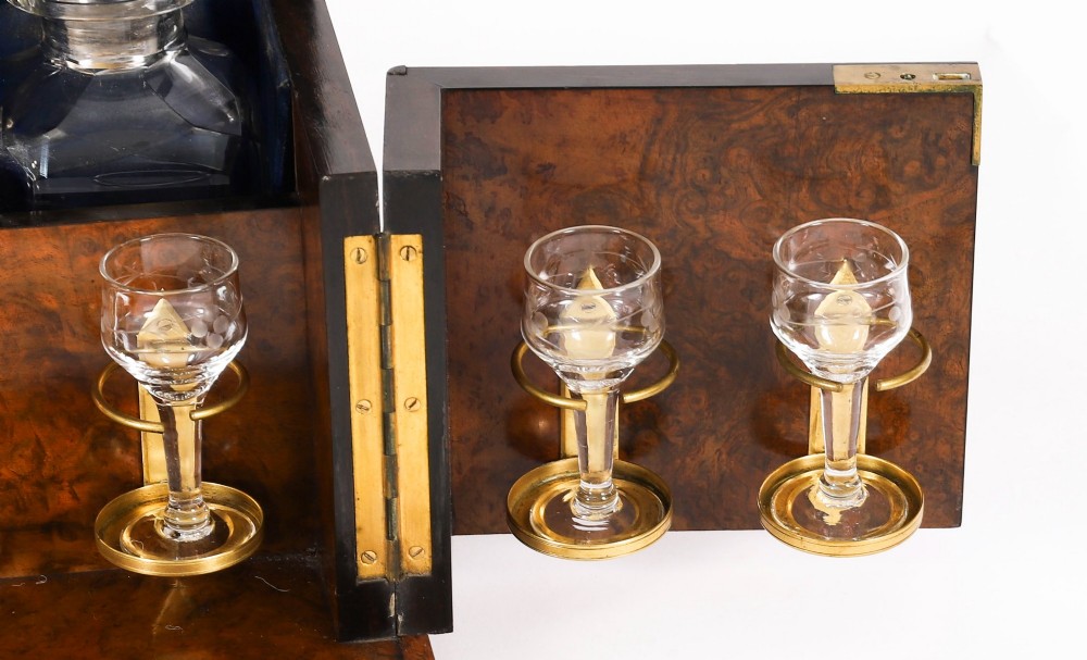 An open and closed 19th-century Victorian burr walnut tantalus box containing three cut crystal decanters, brass-mounted liqueur glasses, and a deep blue velvet lining. View V