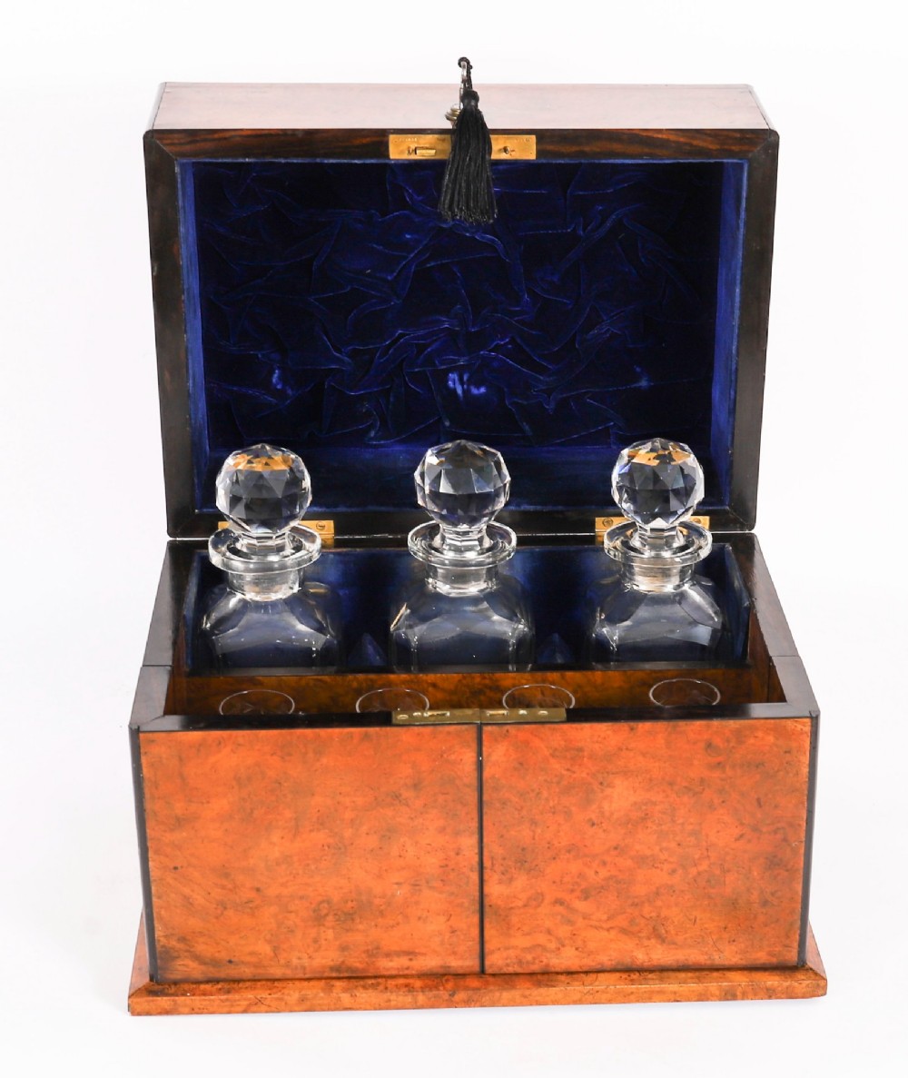 An open and closed 19th-century Victorian burr walnut tantalus box containing three cut crystal decanters, brass-mounted liqueur glasses, and a deep blue velvet lining. View VI