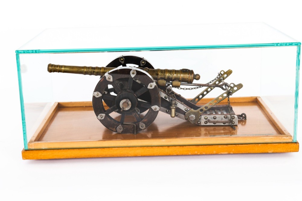 A 19th-century bronze model cannon mounted on a dark wooden carriage and enclosed within a clear glass display case.