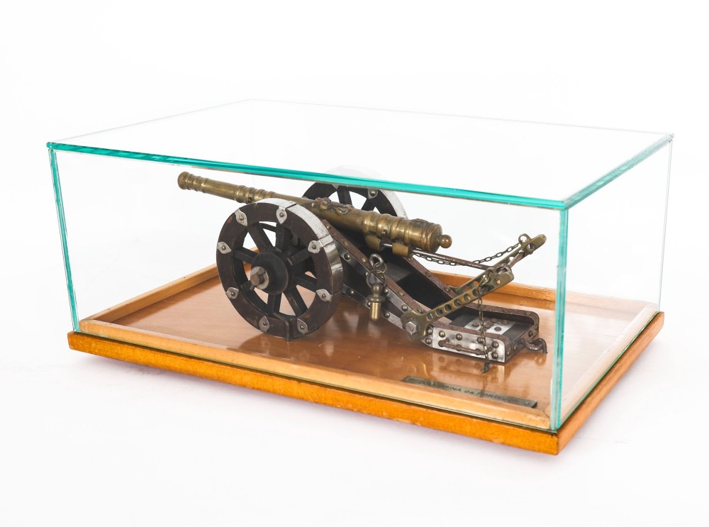 A 19th-century bronze model cannon mounted on a dark wooden carriage and enclosed within a clear glass display case. View II