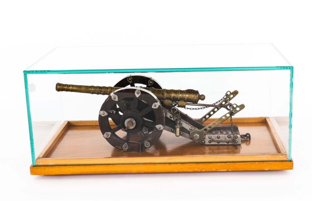 A 19th-century bronze model cannon mounted on a dark wooden carriage and enclosed within a clear glass display case. View IV