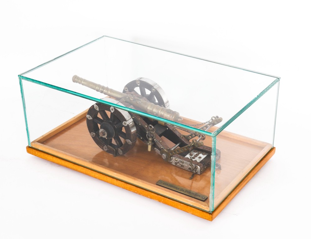 A 19th-century bronze model cannon mounted on a dark wooden carriage and enclosed within a clear glass display case. View VIII