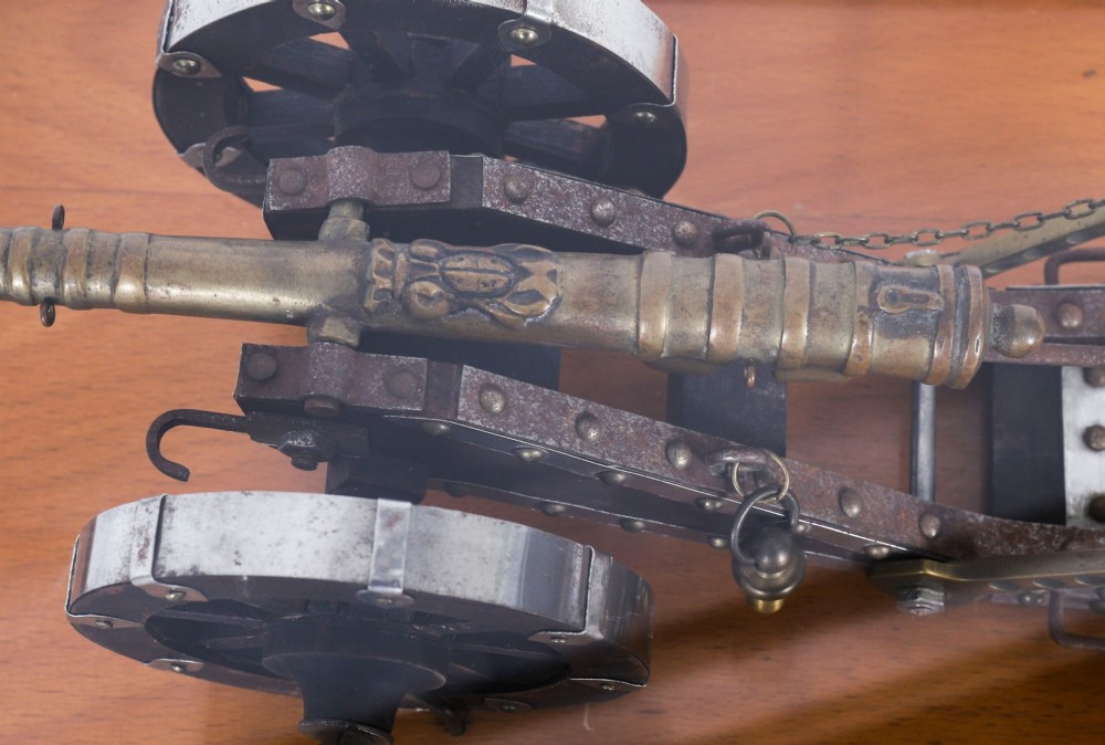 A 19th-century bronze model cannon mounted on a dark wooden carriage and enclosed within a clear glass display case. View X