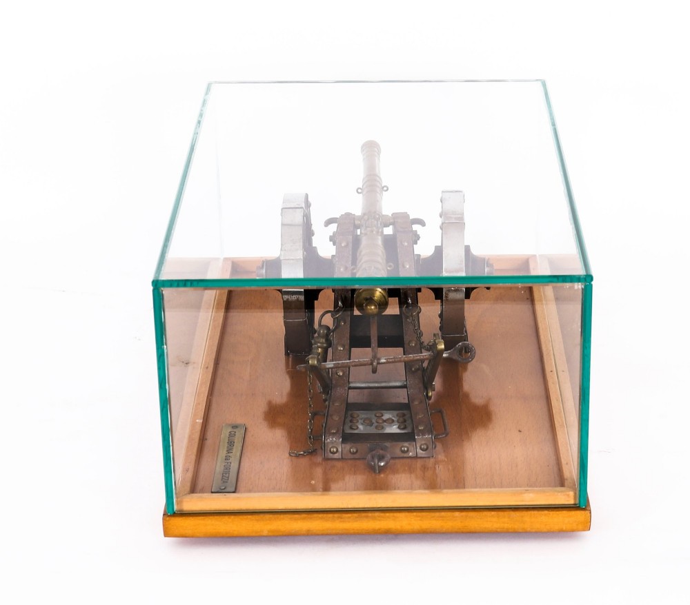 A 19th-century bronze model cannon mounted on a dark wooden carriage and enclosed within a clear glass display case. View XI