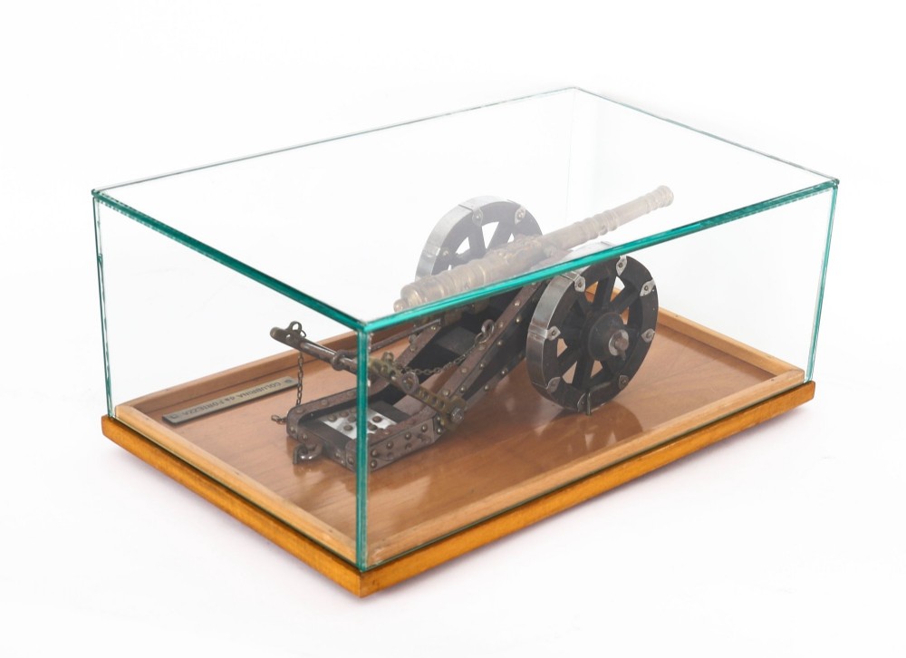 A 19th-century bronze model cannon mounted on a dark wooden carriage and enclosed within a clear glass display case. View XII