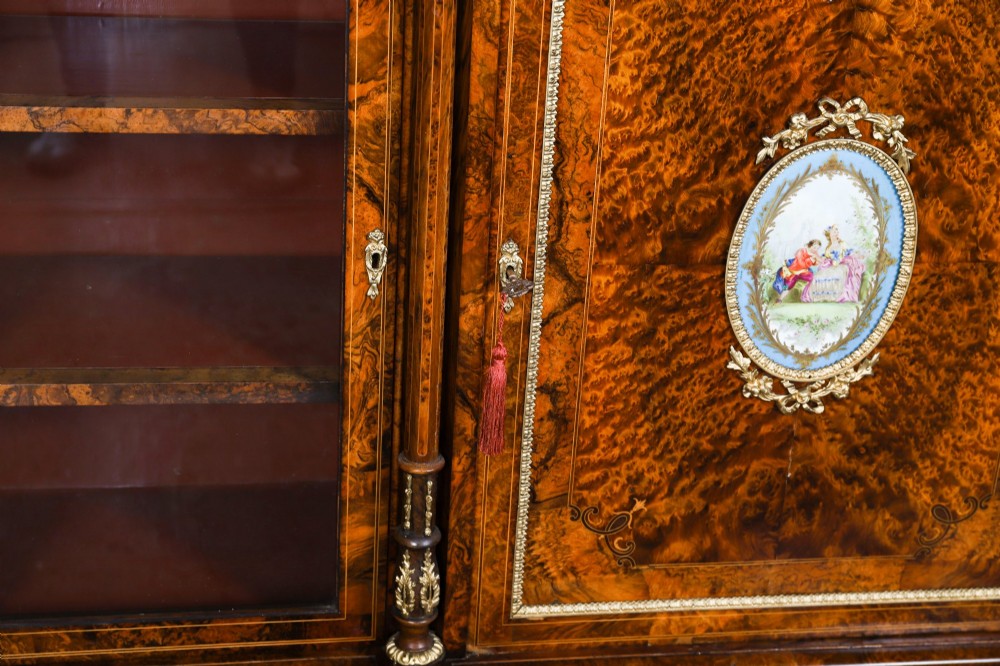 A nineteenth-century Victorian burr walnut credenza featuring an arched mirror back, glazed side doors, and a central cupboard inlaid with a porcelain plaque. View XIII
