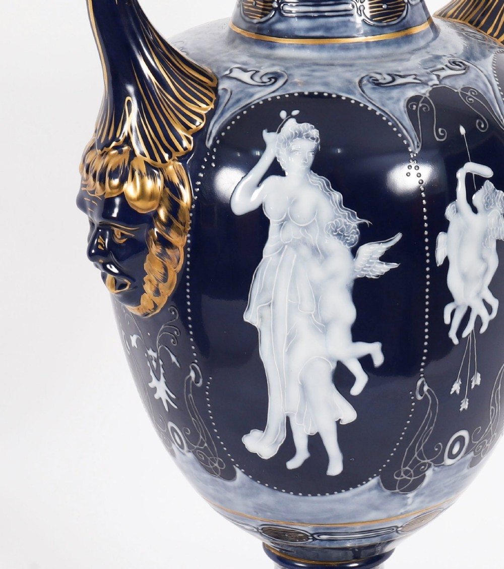 A pair of cobalt blue and white porcelain lidded vases featuring classical figures, scrolling handles, and gilded finials. View X