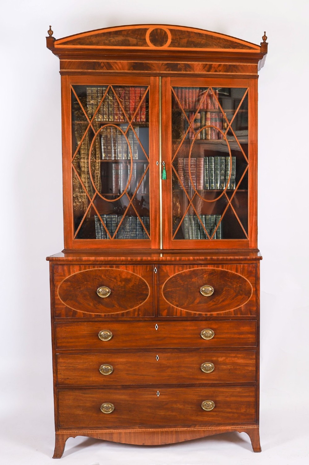 An antique George III flame mahogany secretaire bookcase featuring a shaped pediment, two upper astragal glazed doors, and a lower four-drawer chest base with brass ring handles.