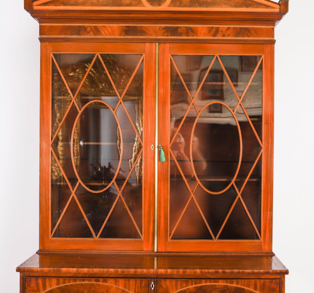 An antique George III flame mahogany secretaire bookcase featuring a shaped pediment, two upper astragal glazed doors, and a lower four-drawer chest base with brass ring handles. View V