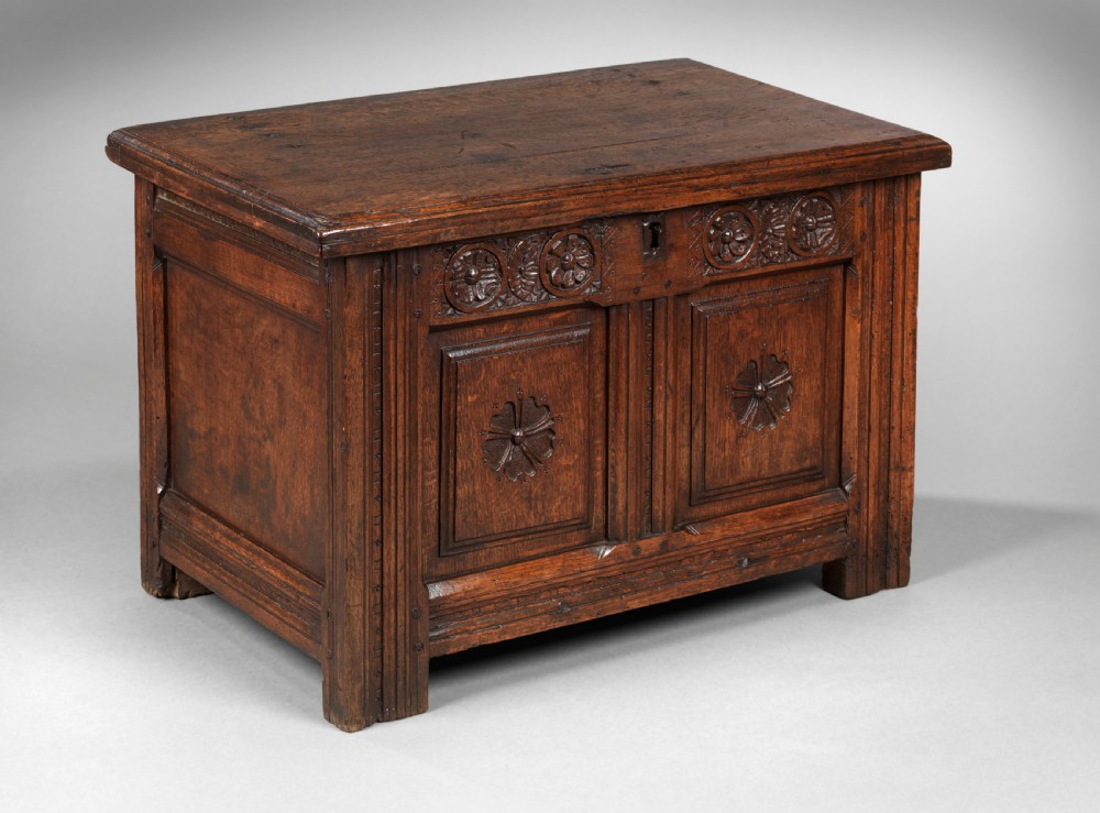 A small 17th-century Charles II carved oak coffer featuring carved floral rosettes, panelled front, and a dark waxed finish. View II