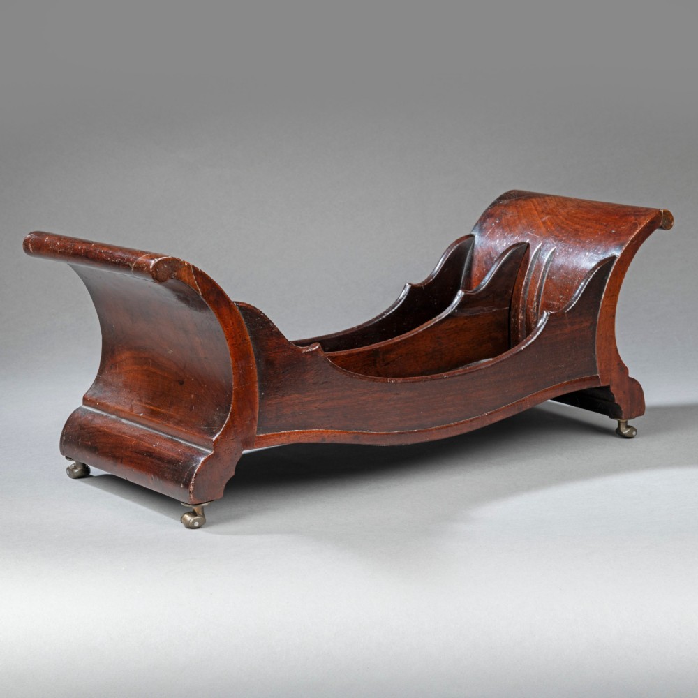 A Georgian mahogany cheese coaster featuring a curved boat-shaped form with internal dividers, scrolled ends, and small brass castors on the base. View II