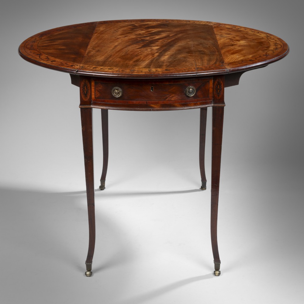 A Georgian mahogany oval Pembroke table featuring marquetry inlay around the perimeter, a single drawer with brass ring handles, and slender square tapered legs fitted with brass castors.