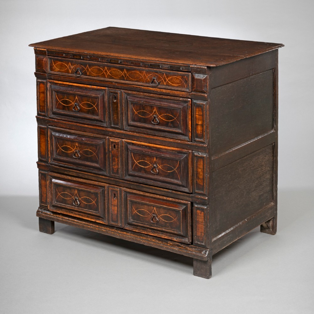 A seventeenth-century dark oak chest of drawers featuring geometric oyster veneer inlay, moulded drawer fronts, and drop handles.
