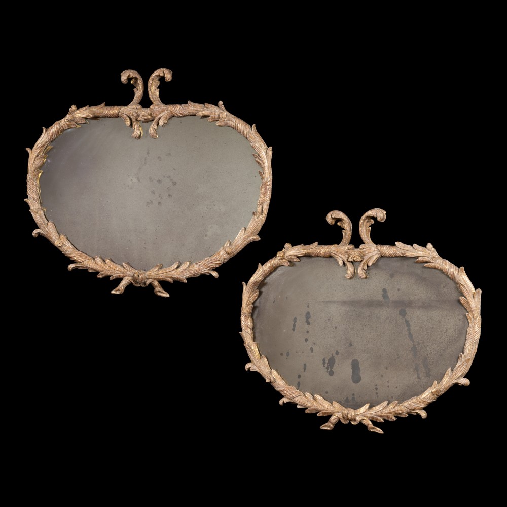 A matching pair of horizontal oval Georgian giltwood mirrors featuring carved leafy scrollwork frames and aged glass.