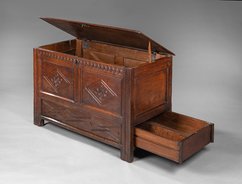A seventeenth-century carved oak coffer featuring geometric lozenge panel carvings and a dark polished timber finish. View II