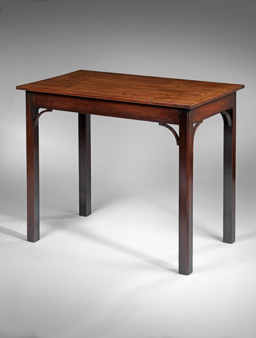 An 18th-century Chippendale period mahogany centre table featuring straight square legs with curved corner spandrels and a smooth rectangular top.