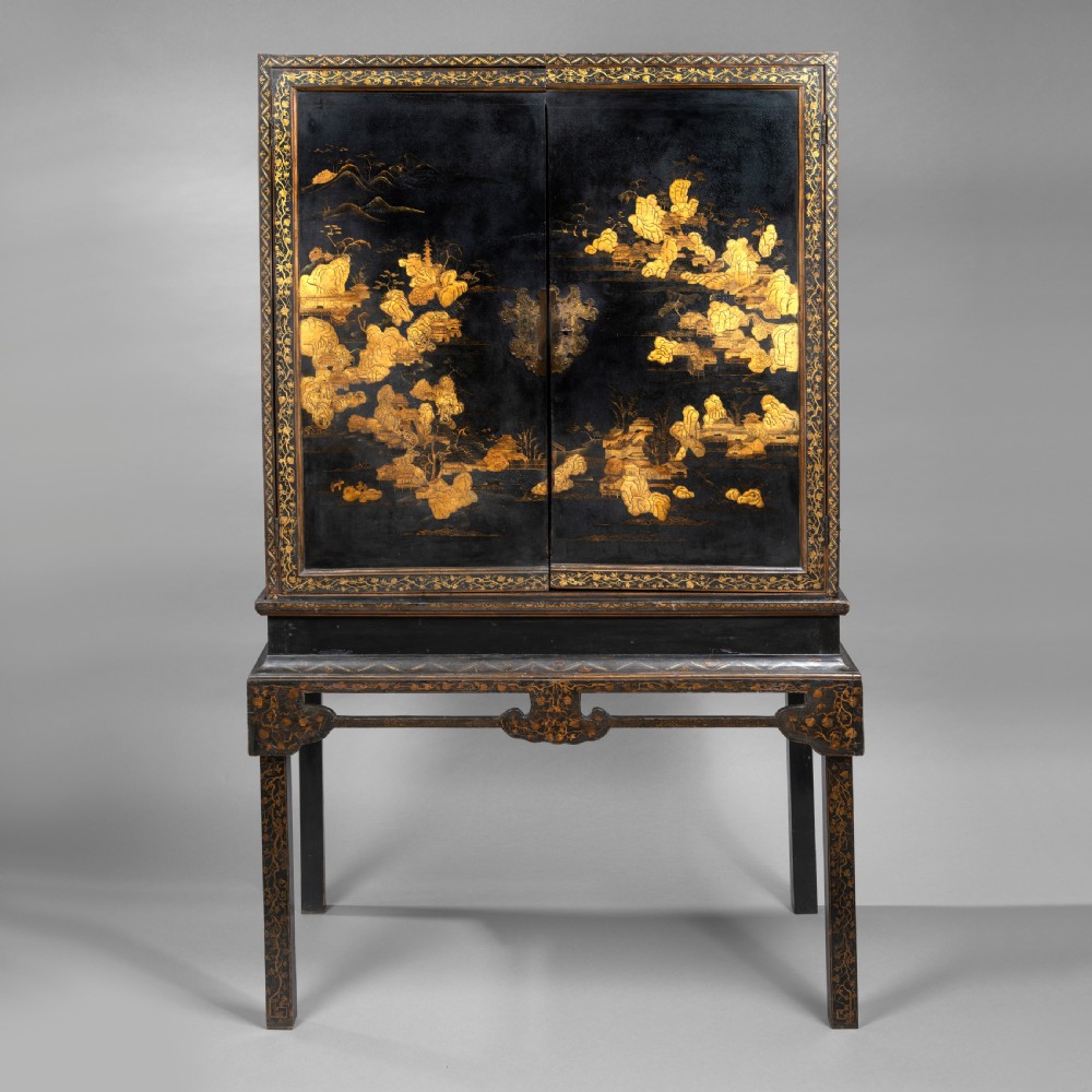 A 19th-century Chinese black lacquer cabinet decorated with intricate gilt landscapes, mounted on a matching tall table stand.