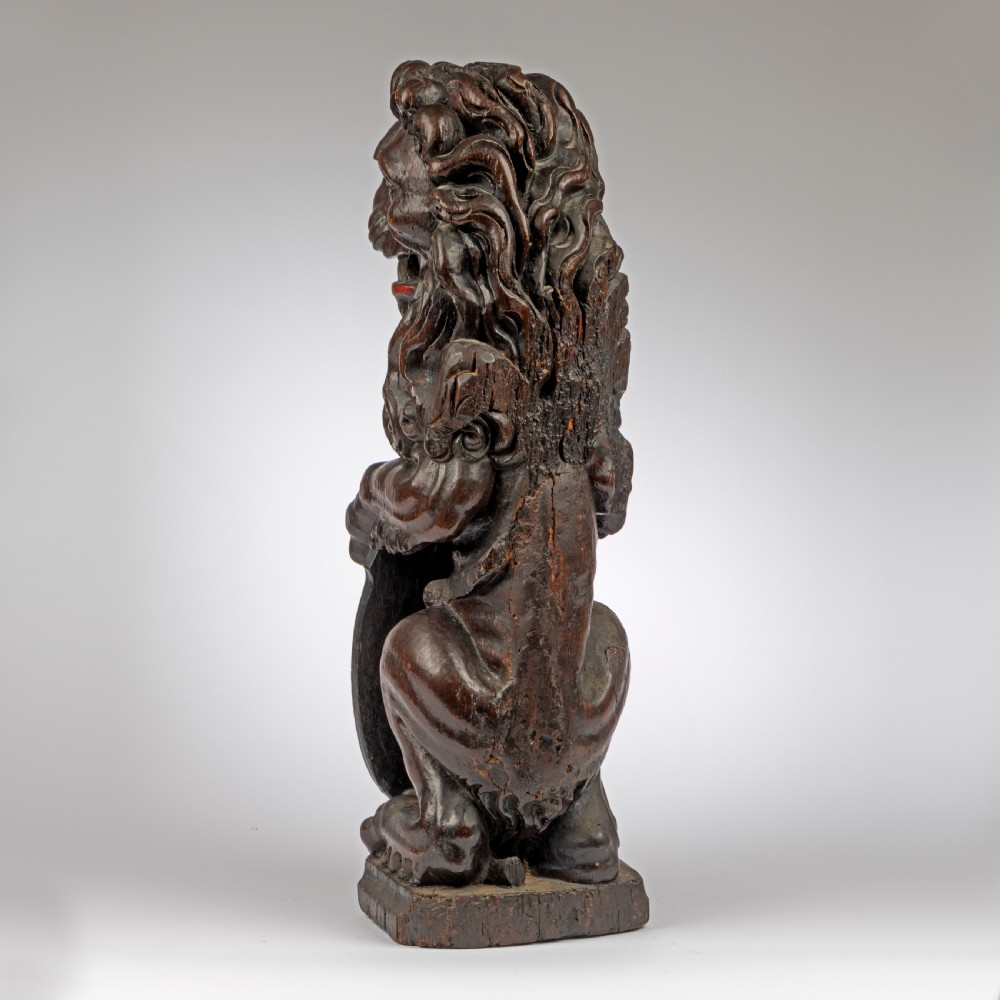 A seventeenth-century dark carved oak lion newel post finial seated upright while holding a painted heraldic shield with yellow, red, and black coat of arms details. View III