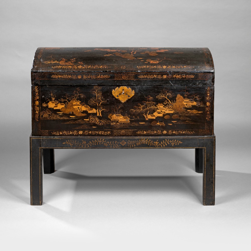 An eighteenth-century black lacquer coffer featuring gold chinoiserie landscape paintings, resting on a matching wooden stand.