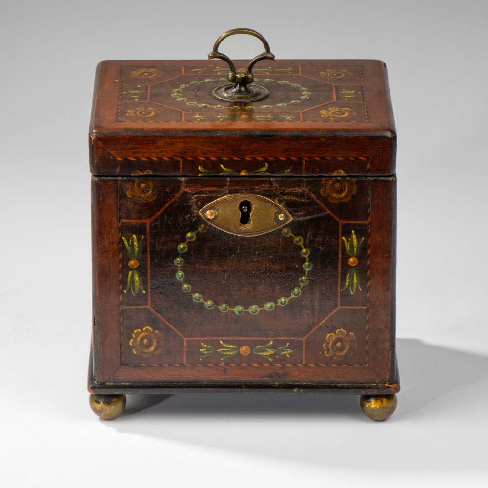 A square dark warm brown mahogany tea caddy featuring hand-painted floral motifs, a brass keyhole escutcheon, a brass top handle, and four small ball feet.