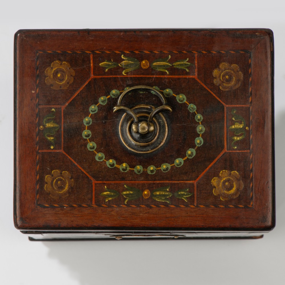 A square dark warm brown mahogany tea caddy featuring hand-painted floral motifs, a brass keyhole escutcheon, a brass top handle, and four small ball feet. View II
