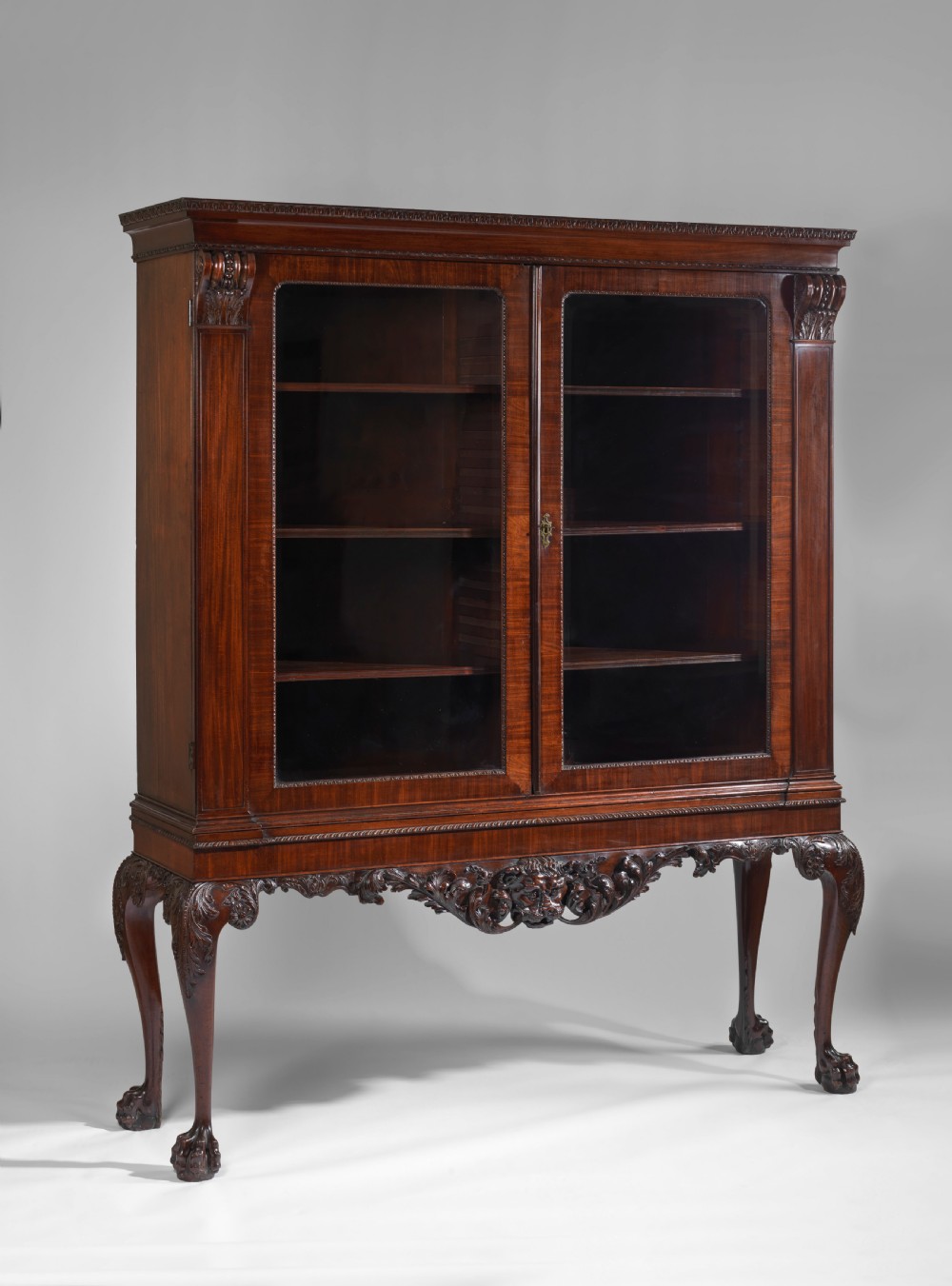 A dark mahogany George II style display cabinet on stand featuring glazed double doors, a carved apron with central mask detail, and cabriole legs with claw and ball feet. View II