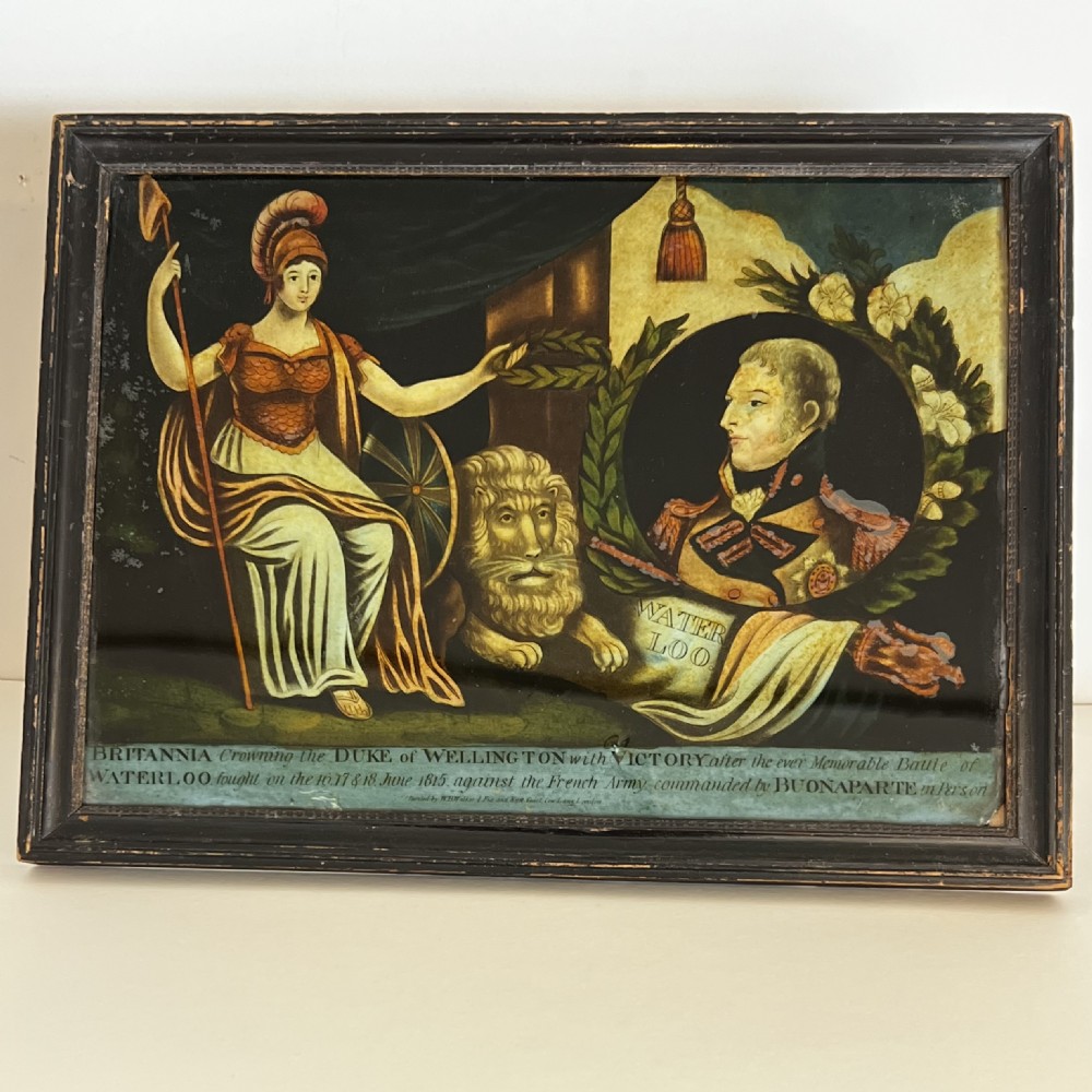 A framed 19th-century reverse glass print depicting Britannia crowning the Duke of Wellington alongside a lion and military motifs in a dark wooden frame.