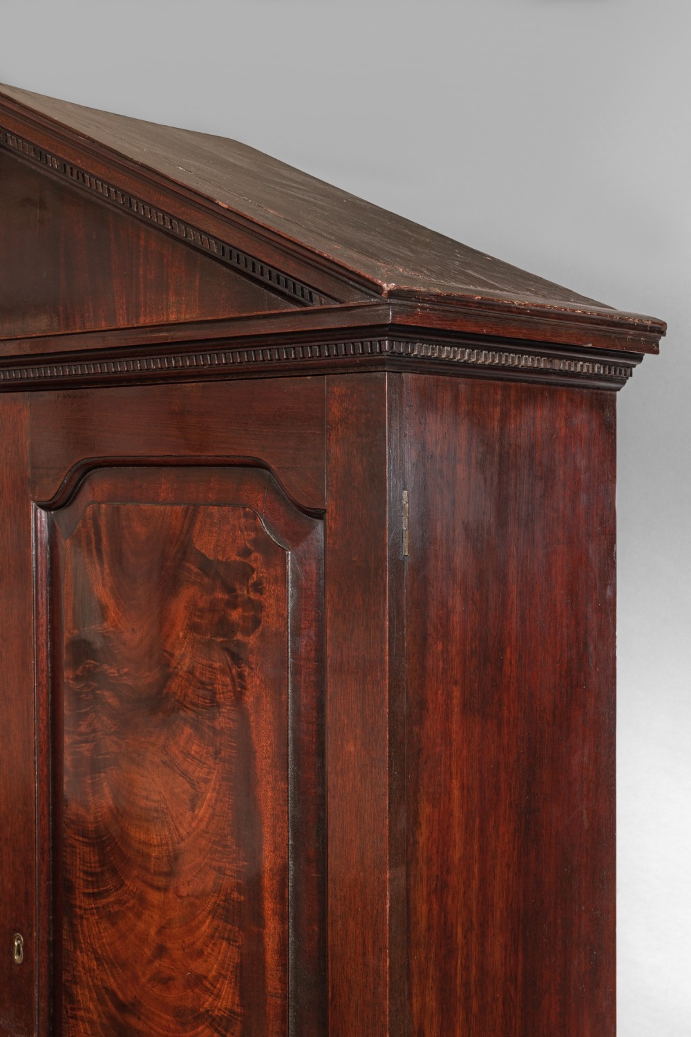 An antique Georgian mahogany linen press featuring a pediment top, two panelled doors with flame mahogany veneer, three drawers below, and bracket feet. View III