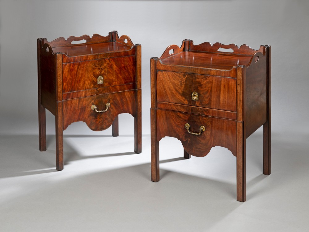 A pair of Georgian Chippendale mahogany tray top commodes featuring pierced side handles, galleried rims, flame mahogany fronts, and brass handles on square legs.