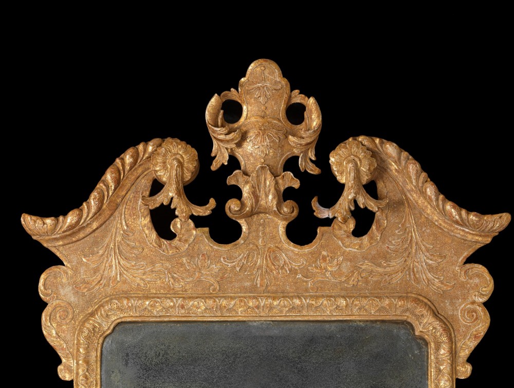 An eighteenth-century George II carved gilt gesso wall mirror featuring an architectural pediment with cresting, low-relief floral patterns, foxed mirror glass, and two brass candle sconces at the base. View II
