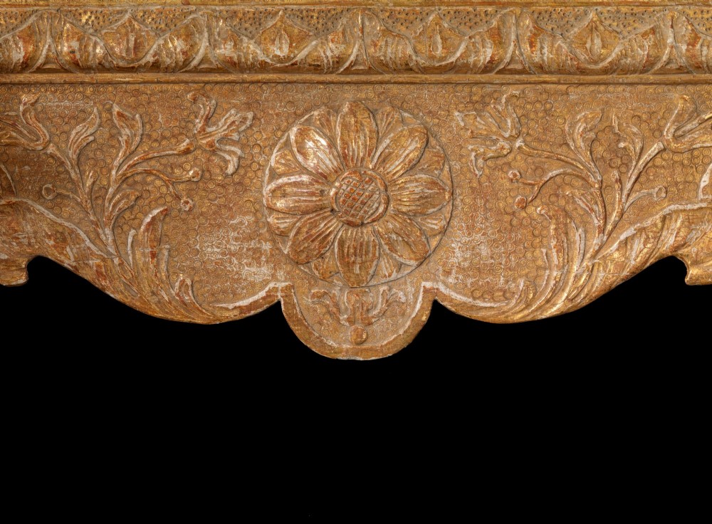 An eighteenth-century George II carved gilt gesso wall mirror featuring an architectural pediment with cresting, low-relief floral patterns, foxed mirror glass, and two brass candle sconces at the base. View III
