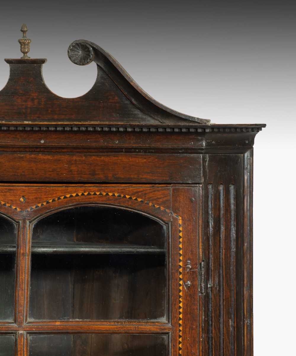 An 18th-century Georgian dark oak corner cupboard featuring a swan-neck pediment, glazed upper door panels, and decorative inlay motifs. View III